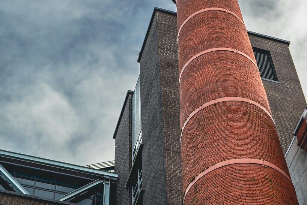 Low angle view of a brick industrial chimney and building against a cloudy sky, showcasing urban architecture.